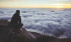 Man sitting above the clouds looking across valley at sunrise